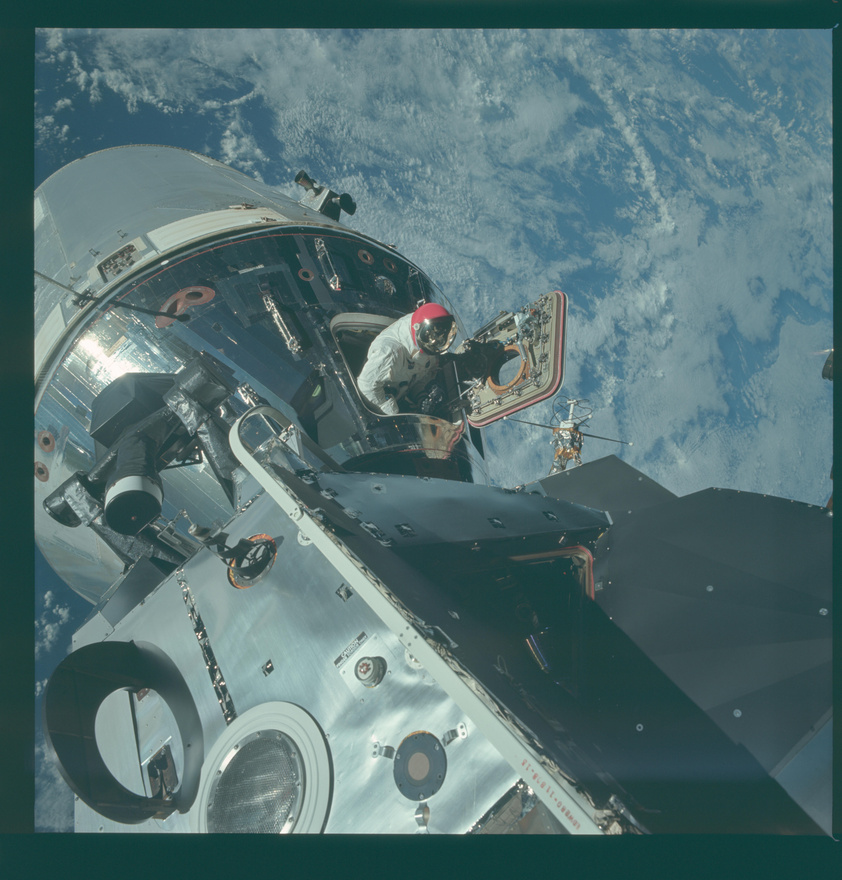 Dave Scott mászik ki az űrhajóból a 9-es Apollo-küldetéskor. Scott az anyahajó parancsnoka volt, és amit látunk, az az űrséta egyszerűsített formája, amikor az űrhajós nem hagyja el a zsilipet, csak kiemelkedik rajta, például hogy fényképezzen. A kép további érdekessége a piros sisak: az Apollo-9 nem ment el a Holdig, ezért nem a közismert fehér sisakot használták, már csak azért sem, mert azt épp ekkoriban fejlesztették. Ez a piros sisak átmenet volt a félig fém, félig üveg sisakok, és az átlátszó üvegbuborék sisakok között.