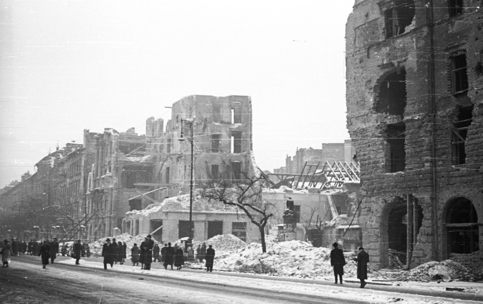 A Nagykörút és az Üllői sarka másik szögből. A piszkosfehér hófoltokból is látszik, hogy a kép később készült, de a pusztítás is egyértelművé teszi, hogy a nagyobb, november 4-5-ei szovjet támadás után vagyunk. A kép közepén látható romok annak a bérpalotának (Üllői út 49-53.) a maradványai, amelynek az előző fotón még csak az egyik frontfala hiányzott.