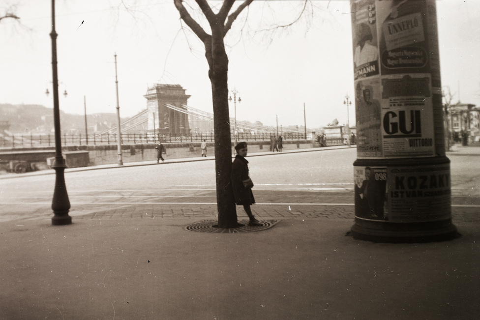 Hirdetőoszlop a Lánchíd pesti hídfőjénél. A fának támaszkodó gyerek alatt egy legalább olyan ikonikus budapesti utcaelem van, mint amilyen az oszlop: a fák földtányérját védő vasrács. Ezen az 1941-es fényképen épp úgy néz ki, mint Fromm Géza 1894-es térhatású fotóján a Nagykörúton, vagy a mai Pesten bárhol.