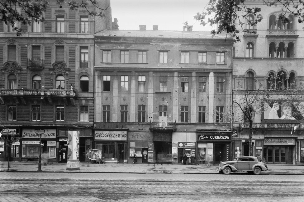 Egy évvel korábban még katonaruhákkal volt tele a város, ezen a fotón viszont már a Bakaruhában című, új magyar film plakátjait láthatjuk az Uránia mozi bejárata fölött éppúgy, mint a hirdetőoszlopokon. Ugyanebben az évben, 1957-ben alakul meg amúgy a Mahir, a Magyar Hirdető is.