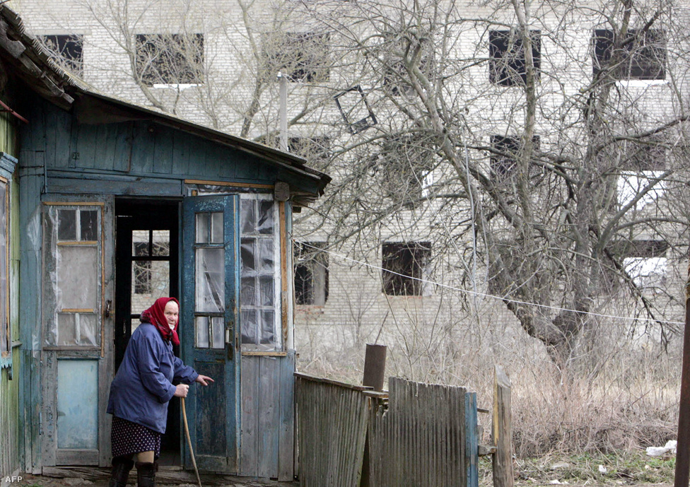 Egy idős nő áll a háza előtt 2006 áprilisában, a belarusz Sztrelicsevo falujában, mindössze pár kilométerre a 30 kilométeres zónától.  1986-ban a települést önkéntes alapon kiürítették, aztán lassanként visszaköltöztek az emberek: főleg oroszul beszélő emigránsok Ázsiából. A kormány hirdetésekkel csábította ide az embereket, akik közül sokan csak érkezéskor jöttek rá, mi vitte el innen az egykori lakosokat. Eredetileg 84 család költözött ide. Mivel pont a zóna határán vannak, nagyjából működik a civilizáció, hozzájutnak például áramhoz. Anno nagyon jól hangzott, hogy az akkoriban modernnek számító szovjet technológiát, traktorokat kapnak a földek megműveléséhez. 