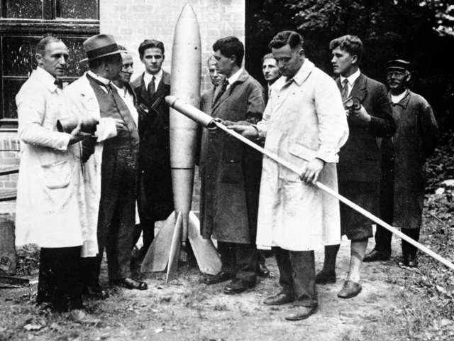 Az őrült rakétások (VfR) tagjai. Rudolph Nebel a bal oldalon, Hermann Oberth, az első elnök a rakétától jobbra, Klaus Riedel, kezében a kis rakétával és mögötte a fiatal Wernher von Braun.