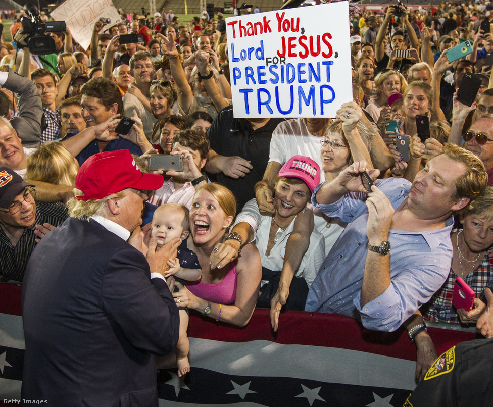 Az egész éves amerikai kampányőrületből ehhez a fotóhoz térek vissza leggyakrabban. Volt egy Nagyképünk, amiben összegyűjtöttük Trump és a legnagyobb rajongóinak intenzív találkozásait, de ez a fotó még abban a válogatásban is kilóg a sorból. Trumpot csak hátulról-profilból és a jellegzetes haja nélkül látjuk, a kép mégis csak róla szól igazán. Hisztéria, vallásos imádat, társadalomrajz - minden egyben ezen a tömegjeleneten. Én a mai napig nem tudtam megfejteni, kihez tartozik az a belógó kar a rózsaszín baseball-sapka mellett.A legtöbben nem sok esélyt adtak volna neki, amikor 2015 
                        nyarán bejelentette az elnökjelölti indulását, de a 
                        milliárdos Donald Trump előbb a republikánusok 
                        jelöltségét söpörte be a pártvezetés 
                        által támogatott jelöltek orra elől, nyerte meg
                         november 8-án az amerikai elnökválasztást a demokrata 
                        Hillary Clinton ellen, hogy számos republikánus vezető 
                        politikus nem volt hajlandó mögé állni. 
                        
                        Trump a kampány során egymás után keveredett botrányos 
                        ügyekbe vitatható húzásai és megszólalásai miatt, 
                        azonban Clintonnak a külügyminiszterként magán 
                        emailszerverén folytatott levelezése körüli botrány 
                        mellett a Clinton Alapítvány körüli ügyekkel is szembe 
                        kellett néznie. Az utolsó pillanatban is előkerülő 
                        emailbotrányon kívül azonban leginkább az számított, 
                        hogy Trump tudta megszólítani  a kiábrándult, 
                        vidéki fehér amerikai szavazókat. Az elnökválasztási 
                        kampányt, és az azóta eltelt időszakot, Trump 
                        kabinetjének kiválasztását Fehér Ház 
                        blogunkban követtük.