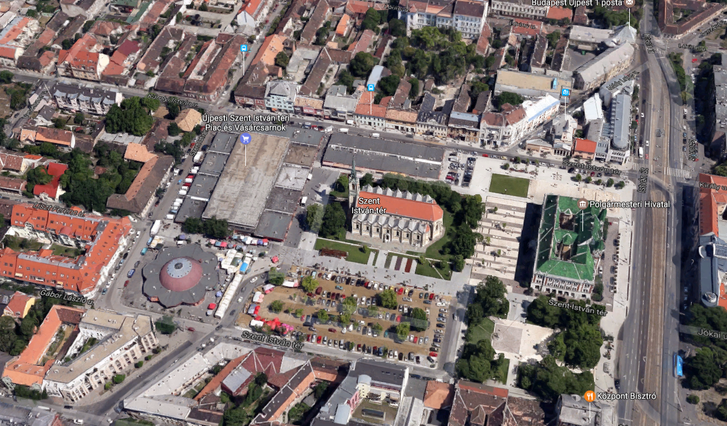 A Szent István tér délről nézve, a Google Maps 2012-es felvételén. Középen a templom, mögötte a városháza, két oldalán a már rendezett térrészekkel. A templommal szemben, és a túloldalán a piac egy-egy csarnoka. A virág alakú épület a Virágpiac. Az új piac a kép bal oldalán látható földszintes házak és a zöld kertek helyére kerül. Cserébe lebontják a mai piacépületeket és oda kerül parkosított tér. Az északi oldalon a buszmegállóval jelzett épület az egykori zeneiskola, ma plébánia. A jobb alsó sarokban a Központ bisztró, ahol remek hamburgert adnak, és ha fehér ingben mész be, egyből hoznak egy plusz szalvétát, amit a nyakadba tűrhetsz, hogy le ne edd magad