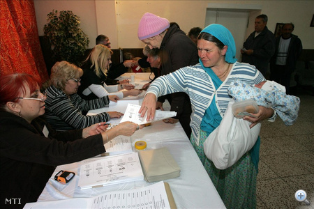 Somogyvámos, 2010. október 3. Majzik Gáborné (babával) és Hosszúné Markó Alexandra (k) Krisna-tudatú hívők átveszik a szavazólapokat Somogyvámoson a kultúrházban felállított 1-es számú szavazókörben a 2010-es önkormányzati választáson. A nyolcszáz lakosú település életét egyre jobban befolyásolhatja a völgyben élő 150 krisnás, akik 3 képviselőjelöltett inditottak. MTI Fotó: Varga György 