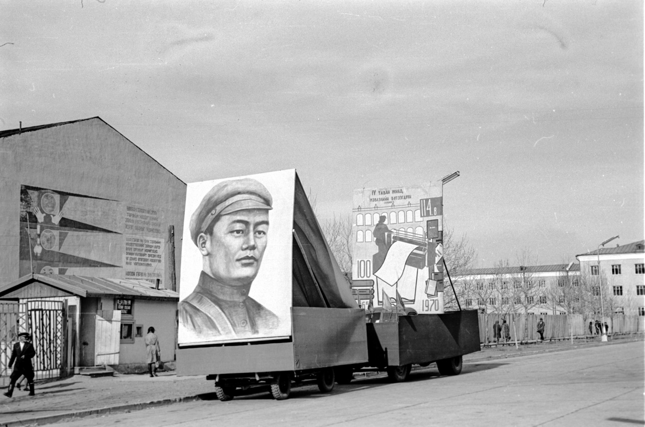 Szühebátor, az 1921-es mongol forradalom vezéralakjának a képe, valamint "A 4. ötéves terv kiadványai" beszerzésére buzdító felirat. Mongólia a polgárháborús állapotba zuhanó Kínától a huszas években nyerte el bolsevik segítséggel a függetlenségét, a Szovjetunió után ők lettek a világ második szocialista állama. A fotó az ugyancsak Szühebátorról elnevezett nyomda előtt készült. Bár az egykor szintén az ő nevét viselő ulánbátori főteret a rendszerváltás után átkeresztelték Dzsingisz kánra, a szocialista államalapító téren álló szobrát nem bántották, az áll ma is, ahogy a kultusza sem enyészett el a kurzusváltás ellenére sem.