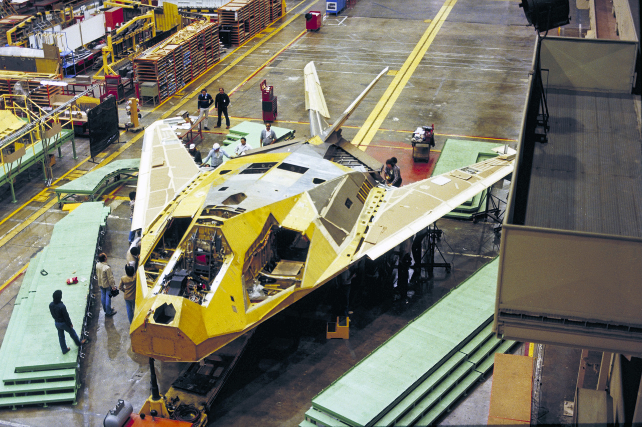 1980. Ez itt az első F-117 Nighthawk lopakodó repülőgép (légierő sorozatszáma: 79-10780) az összeszerelés utolsó fázisában, a Lockheed Skunk Works burbanki telephelyén. Első körben öt F-117-est építettek, amikkel a típus teljesítményét, stabilitását, irányíthatóságát és rendszereit tesztelték. A tesztgépeket a legnagyobb titokban, éjszaka vitték el C-5-ös szállítógépekkel a gyárból. Az első repülésre 1981. június 18-án került sor, de a lopakodók létezéséről 1988. november 10-ig nem lehetett tudni semmit. A képen látható repülőgép jelenleg a nevadai Nellis légibázison van kiállítva.