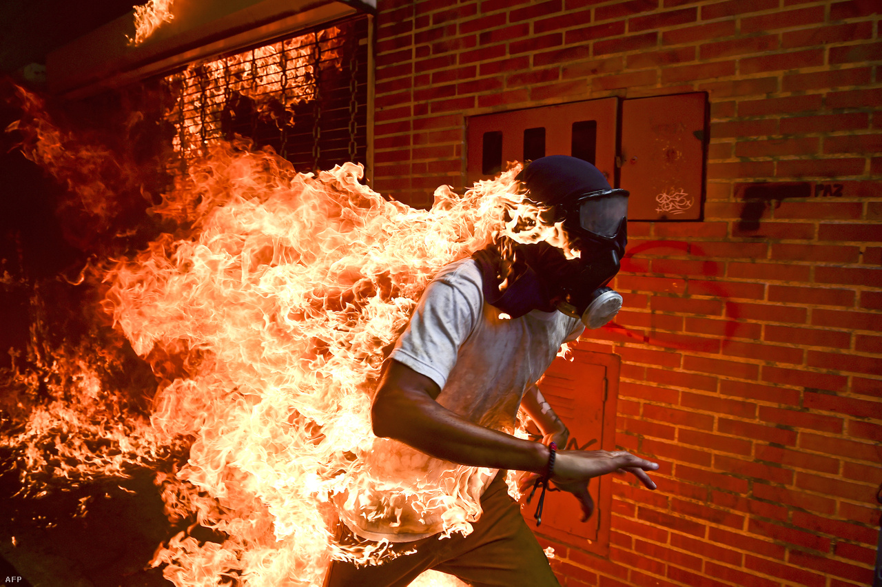 Venezuelai tüntetők csoportja kövekkel dobált egy felgyújtott rendőrmotort, amikor jármű üzemanyagtartálya felrobbant. A motor mellett álló tüntető ruhája lángra kapott, a körülötte állók pedig vízzel és rongyokkal próbálták eloltani. A néhány másodpercig tartó brutális jelenetet az AFP hírügynökség két fotósa is megörökítette. A képsorozatot tavaly az Indexen is láthatták.