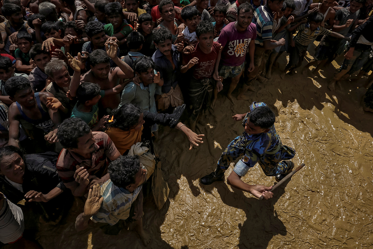 Segítségre váró menekülteket próbál visszatartani egy rendőr egy Banglades melletti gyűjtőpontnál. 