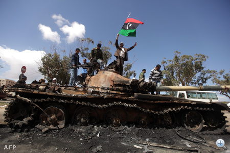 Felkelők lengetik a líbiai zászlót Kadhafi hadseregének kilőtt tankján