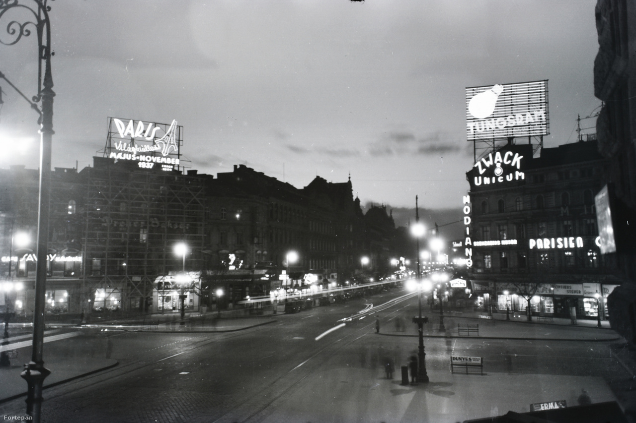 1937 körül készülhetett ez a körfotó, legalábbis bal oldalt a Párizsi Világkiállítás neonreklámja erre utal. A teret a Tungsram hatlamas tetők fölé magasodó neonja uralja, a Zwack unicum és a Modiano cigaretta reklámja fölött. A margitszigeti Parisien Grill Revue Dancing mulató neonja szenzációs műsort ígér. Balra lent a Savoy Kávéház neonja látható még.
