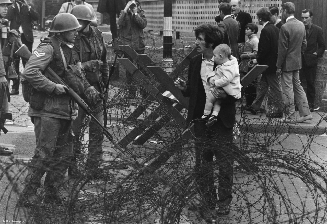 Brit katonák állítják meg a gyermekével átkelni szándékozó férfit a szögesdrótoknál. A férfi a belfasti Falls Road-on, a katolikus negyed barikádjánál próbálkozott (1969).