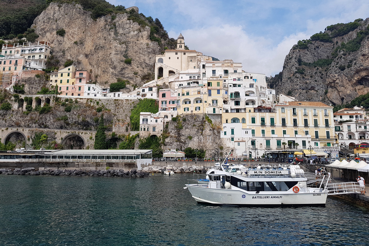 Amalfi kikötője. Maga a városka véleményem szerint kevesebb időt érdemel, mint a pezsgő, izgalmas Positano, ám a kettő közötti hajóutat vétek kihagyni. Ezek elfogadható sűrűséggel járnak, vízen is el lehet jutni idáig, akár Nápolyból is, de Capri szigete is egyszerűen elérhető innen. Brutális sziklák, rejtett öblök, eszméletlen épületek, tényleg a világ egyik legszebb partvidéke