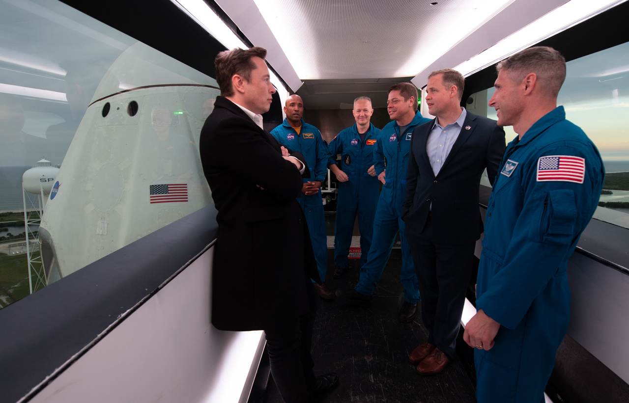 Elon Musk, a SpaceX tulajdonosa, fő tervezője és igazgatója (bal szélen) március 1-jén a NASA igazgatójával, Jim Bridenstine-nal valamint négy NASA-űrhajóssal (Victor Glover, Doug Hurley, Bob Behnken, Mike Hopkins) a startállás karjában egyeztetnek az előttök álló Demo-1 küldetésről.
