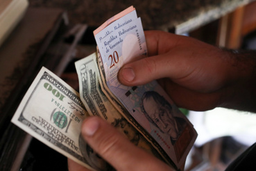 Dollárral és venezuelai bolivar bankjegyekkel fizet egy vásárló a pékségben Caracasban 2019. március 10-én