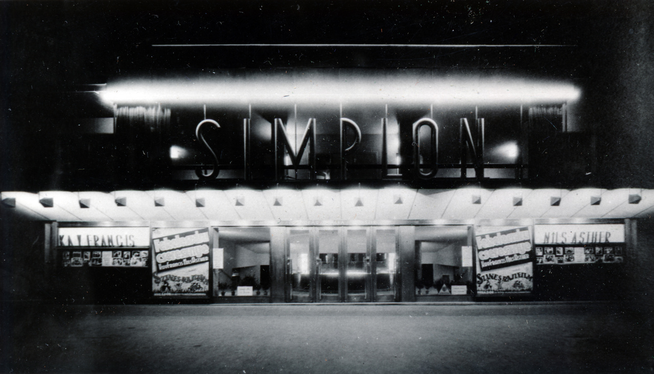 Ez pedig a ház aljában működő mozi bejárata, a SIMPLON felirattal. Érdekes, hogy teljesen más betűtípust használtak itt, mint a tetőn. Akár csak az Excelsior neonjainál, a Simplonnál sem törekedtek egységes arculatra.