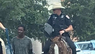 Két fehér rendőr lovon ülve, vezetőszáron vonszol maga után egy bilincsbe vert fekete férfit