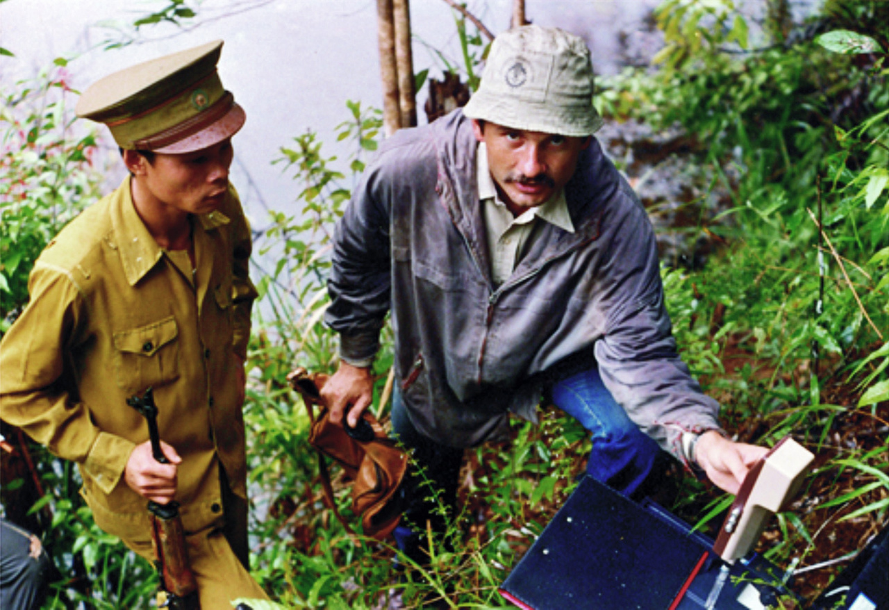 A Földtani Intézet 1985–87 között szervezett egy bauxitkutató expedíciót a dél-vietnámi Bao-Lok–Dilinh körzetben lévő Than Rai bauxit-előfordulás megkutatására. Ennek keretében egy kisebb, geológusokból és vegyészekből álló csoport utazott Vietnámba, ahol 1200 négyzetkilométernyi területen végeztek bauxitkutatást, nyersanyag-minősítő értékeléssel és készletszámítással. A terepi kiszállások itt sem zajlottak egyszerűen. A képen éppen pH-mérés zajlik, fegyveres biztosítással.
