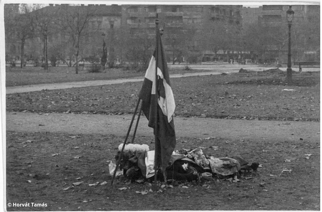 Szintén a Köztársaság tér: elesett felkelő letakart holtteste lukas zászlóval, halottak napi krizantémmal.