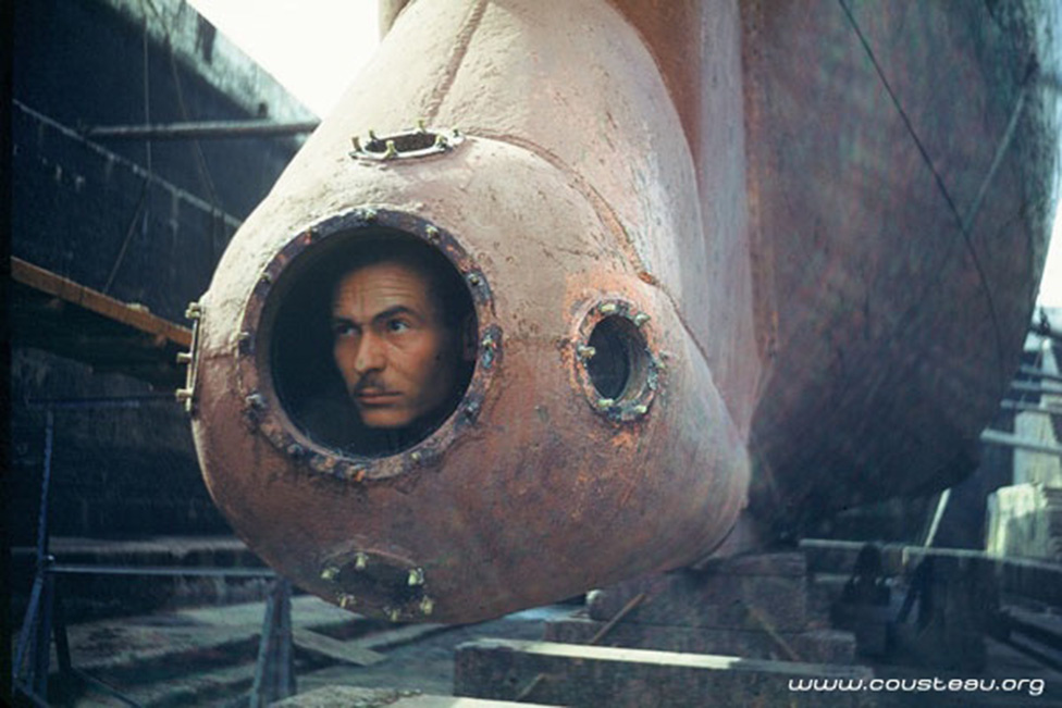 Cousteau a Calypso speciális megfigyelőállásában: az eredetileg aknakereső hajóként szolgáló járművet a kutató tervei alapján alaposan átalakították, például ez a 3 méterrel a vízszint alá nyúló "orr" is utólag került rá.