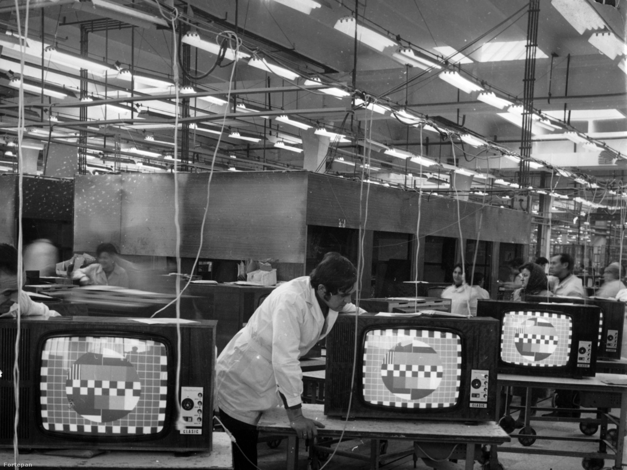 A bukaresti televíziógyár (Electronica)  1960-ban nyitotta meg kapuit, előtte rádiógyár volt. Nem sokkal utána Vasile Cätuneanu, az Electronica gyár főmérnökhelyettese így nyilatkozott az Új Élet termelési riporton lévő munkatársának: "Ha, mondjuk, egy 1700 táján élt ember látná ezt a gyárat, és végignézne egy televíziós adást, az ördöggel való cimboraságért jelentene fel". A kép jóval később, 1980-ban készült. Ekkoriban hatféle készüléket gyártottak a 44 centiméteres képernyő átmérőtől a 65 centiméteresig.