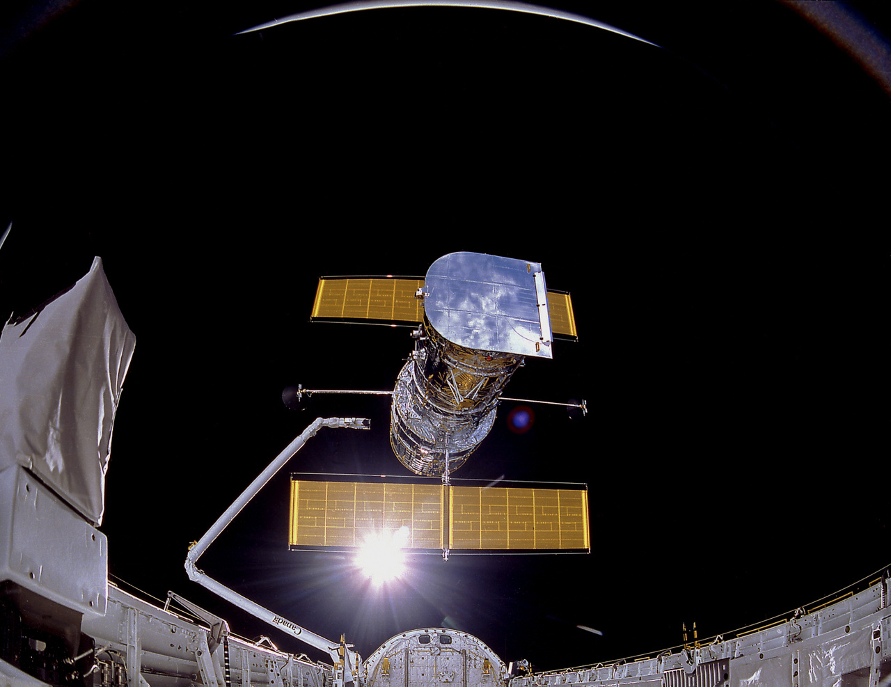 1990. április 25. A Hubble a pályára állítás pillanatában, 614 kilométerrel a Föld fölött. A jellegzetes dupla napelemtáblák már teljesen nyitva, és az űrtávcsövet már nem tartja a Discovery űrsikló mozgatható karja. A csodálatos felvételt IMAX kamerával készítették.
                        