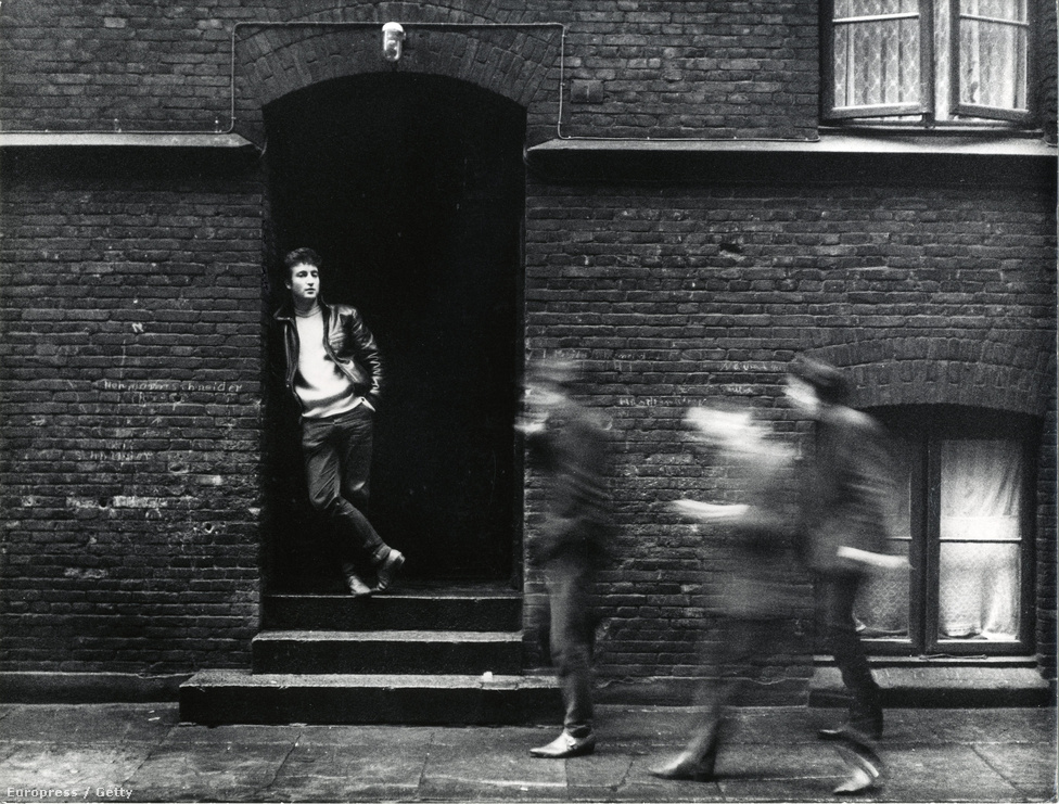 1960-ban John Lennonék a jobb pénzkereseti lehetőségek miatt átköltöztek Hamburgba, ahol már mint The Beatles léptek fel Pete Best dobossal. Ebben az időszakban, de nem itt, hanem Angliában figyelt fel rájuk Brian Epstein menedzser, aki a Stuart Sutcliffe által kitalált bőrdzsekis külsőt lecseréltette a klasszikus, öltönyös-gombafrizurás imidzsre. A kép John Lennont ábrázolja egy hamburgi ajtó előtt 1961-ben.