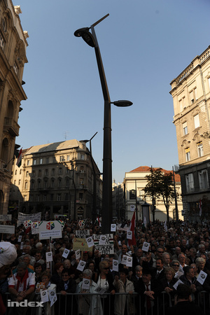 A tömegben magyar zászlók és a DK szervezeteinek táblái láthatók, amik hirdetik, hogy Egerből, Győrből, Várpalotából és Veresegyházáról is vannak itt emberek.