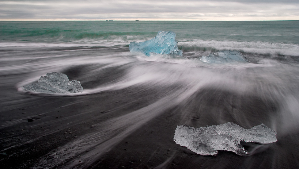 Jeges óceánpart
                        1.díj (Tájak)
                        Izlandi utunk során egy éjszakát töltöttünk Jökursárlón gleccsertava mellett, ami végül az egyik legfagyosabb esténk volt a szigeten – de megérte! A tavat a Brei∂amerkurjökull-gleccser táplálja, és az arról leváló jégtömböket az áramlatok sodorják ki az óceán partjára. A gleccser folyamatosan zsugorodik, régebben lényegében elérte az óceánt, míg napjainkban a vége már csaknem két kilométerre van a parttól. A környék Izland egyik fő látványossága, a tó, a jeges part és a számtalan árnyalatban pompázó jég sokszor szürreális élményt nyújt.
