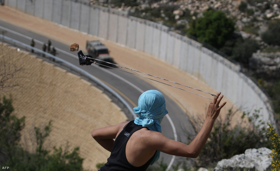 Izraeli járőröket céloz meg parittyájával egy palesztin fiatal Bilin község közelében az Izrealt Ciszjordániával elválasztó falnál április 13-án.