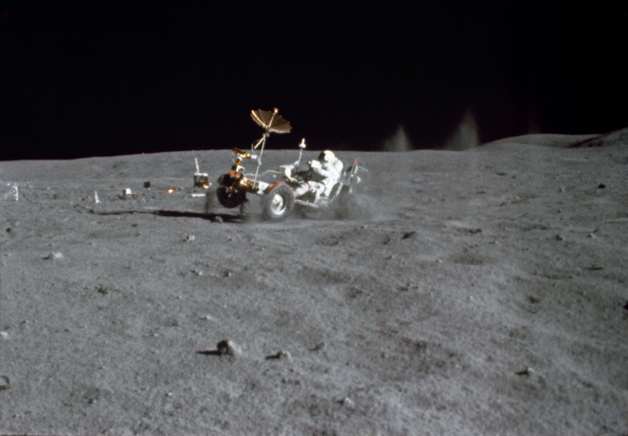 John Young meghajtja a holdjárót az Apollo-16 első holdsétáján, 1972. április 21-én. A fotót egy 16 milliméteres filmre rögzítő speciális Mauer kamera által felvett mozgóképből vágták ki, melyet Charles M. Duke Jr. tartott kezében. A kép érdekessége a felverődő por és kőzet látványa, illetve az, hogy a rover kerekei nem érik a talajt. Az Apollo-16 holdautója fel volt szerelve egyébként egy saját tévékamerával is, de ezt csak megállás után lehetett használni, mert mindig a Föld irányába kellett állnia az átjátszó antennának, hogy fogni tudják a Holdról érkező adást.
                        