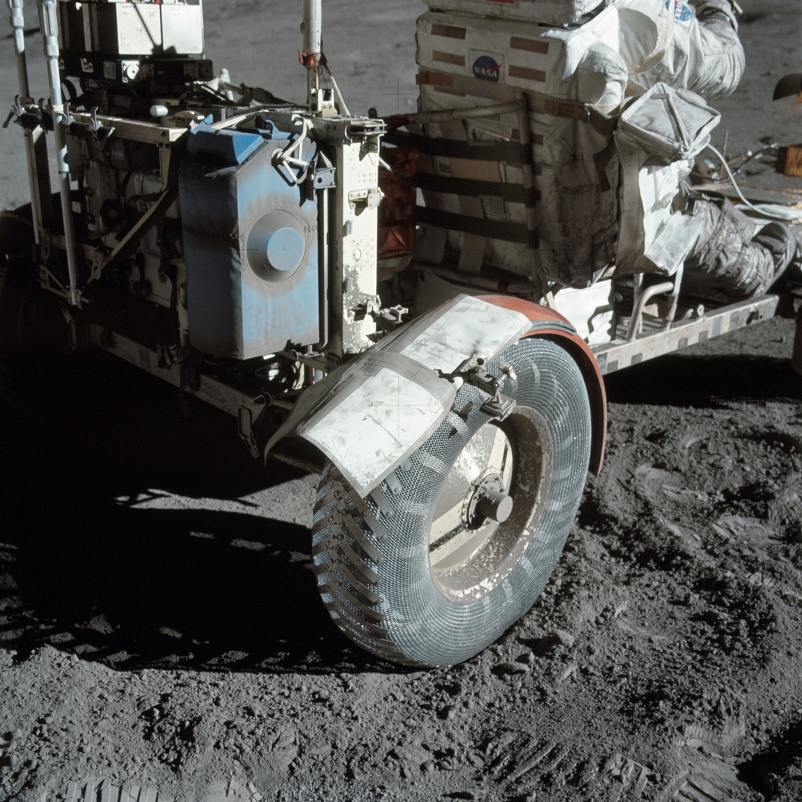 Közeli fotó, ami a sárvédő ideiglenes javításáról készült a Holdon. A NASA először 1999-ben tette közzé a képet az interneten „Holdpor és Ragasztószalag” címmel. A holdautót tartalék térképekkel, fogókkal és ragasztószalaggal kasztnizták. A 38 millió dollárból kifejlesztett járműveket a missziók után nem hozták vissza a Földre, a mai napig a Holdon vannak.
                        