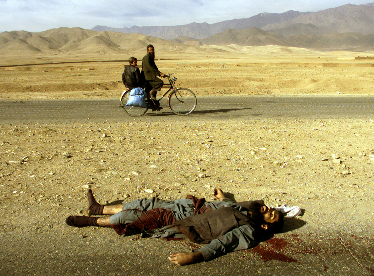 Egy tálib katona holtteste mellett halad el kerékpáron egy afgán családapa fiával. Az iszlamistával a nyugatiak támogatását élvező Északi Szövetség csapatai végeztek. Afganisztán 2001-es megszállása óta becslések szerint több mint 51 ezer tálib katona halt meg az összecsapásokban.
                        Kabul, 2001. november 13.