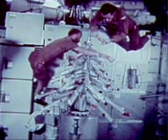 Gerald P. Carr (balra) és Edward G. Gibson (jobbra) a Skylab űrállomás karácsonyfáját állítják fel. A fa üres konzervdobozokból készült, a csúcsdíszt kartonpapírból vágták hozzá.