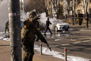 Ukrán katonák egy katonai létesítmény közelében, miközben két autó ég egy kijevi utcán 2022. február 26-án