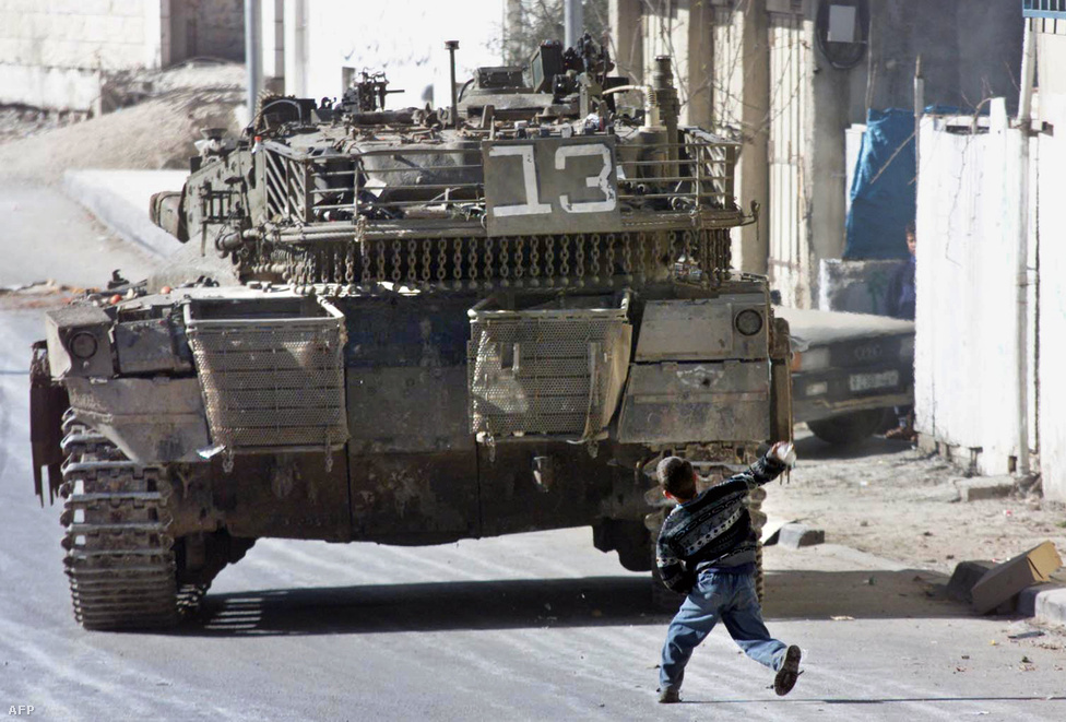 Palesztin fiú dob egy követ egy izraeli tankra a ciszjordániai Hebron városában kirobbant utcai összecsapásokban.