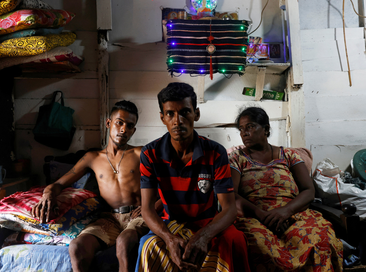 A kép jobbszélén Gamage Rupawathi látható, mellette férje és fiuk. Az asszony arról mesél, hogy a 2020-as járvány előtt jól menő gyümölcsösstandja volt, amiből remekül eléltek. A válságban azonban már nem maradt elég pénze, hogy újraindítsa a vállalkozását. Colombo 2022.08.02.