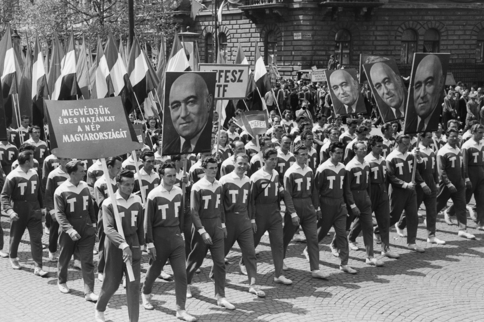 Május elsejei felvonulók az Andrássy úton, a Köröndnél. A tér 1938 és 1945 között Adolf Hitler nevét viselte, 1971-től Kodály körönd. Az Andrássy út a koalíciós időkben nem vesztette el nevét, 1950-ben Szálin út, a forradalom napjaiban Magyar Ifjúság útja, 1957-től Népköztársaság út. A képen a testnevelési főiskolások vonulnak Rákosi Mátyás a kommunista párt főtitkárának portréjával.
                        