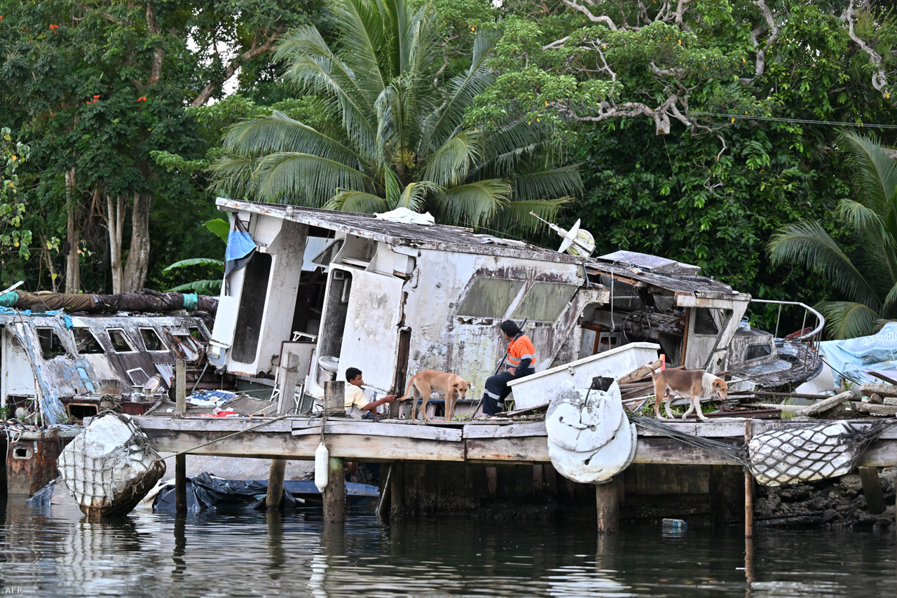 Helyiek üldögélnek egy stégen, egy elhagyott hajócska mellett Suva külterületén. 