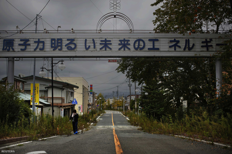 Nukleáris energia: A fényesebb jövő energiája - szól a felirat az üresen álló Futaba városban. Ez a nő egy rövid látogatásra tért vissza régi otthonába, abba a városba, amit a fukusimai atomerőmű tett virágzóvá. A városlakók napjainkban szétszórtan élnek Japán minden részén, és egyáltalán nem tudható, hogy mikor térhetnek vissza a településre.