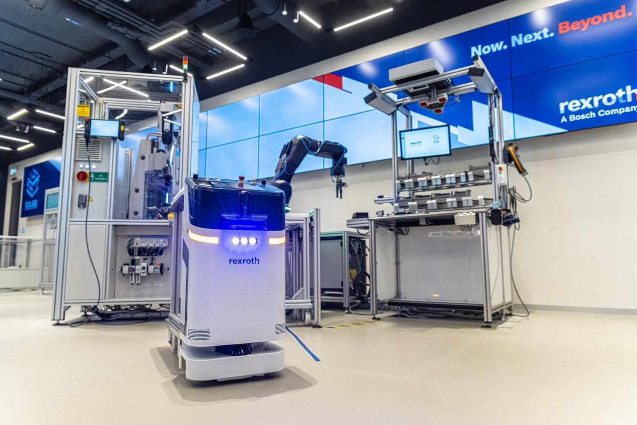 Mivel az automatizált ipari folyamatok másik szegmensét az emberrel együttműködő robotok képviselik, ezért a Bosch Rexroth új kiállítótermében ezek a gépek is helyet kaptak. A fotó előterében látható kis önjáró intralogisztikai robot képes anyagot mozgatni, rendkívül türelmesen kivárja, hogy az emberi akadály elálljon az útjából, és apró érdekesség: a kijelzőjén mosollyal jutalmazza, ha sikerül. A képen a háttérben egy kollaboratív robot látható, amely aktívan támogatja a munkát végző kollégát. A hagyományos ipari robotokhoz képest itt nincs szükség biztonsági kerítésre, miközben a gépek az emberek számára monoton vagy fizikailag különösen megerőltető munkafolyamatokat végzik, egy térben a humán munkaerővel.