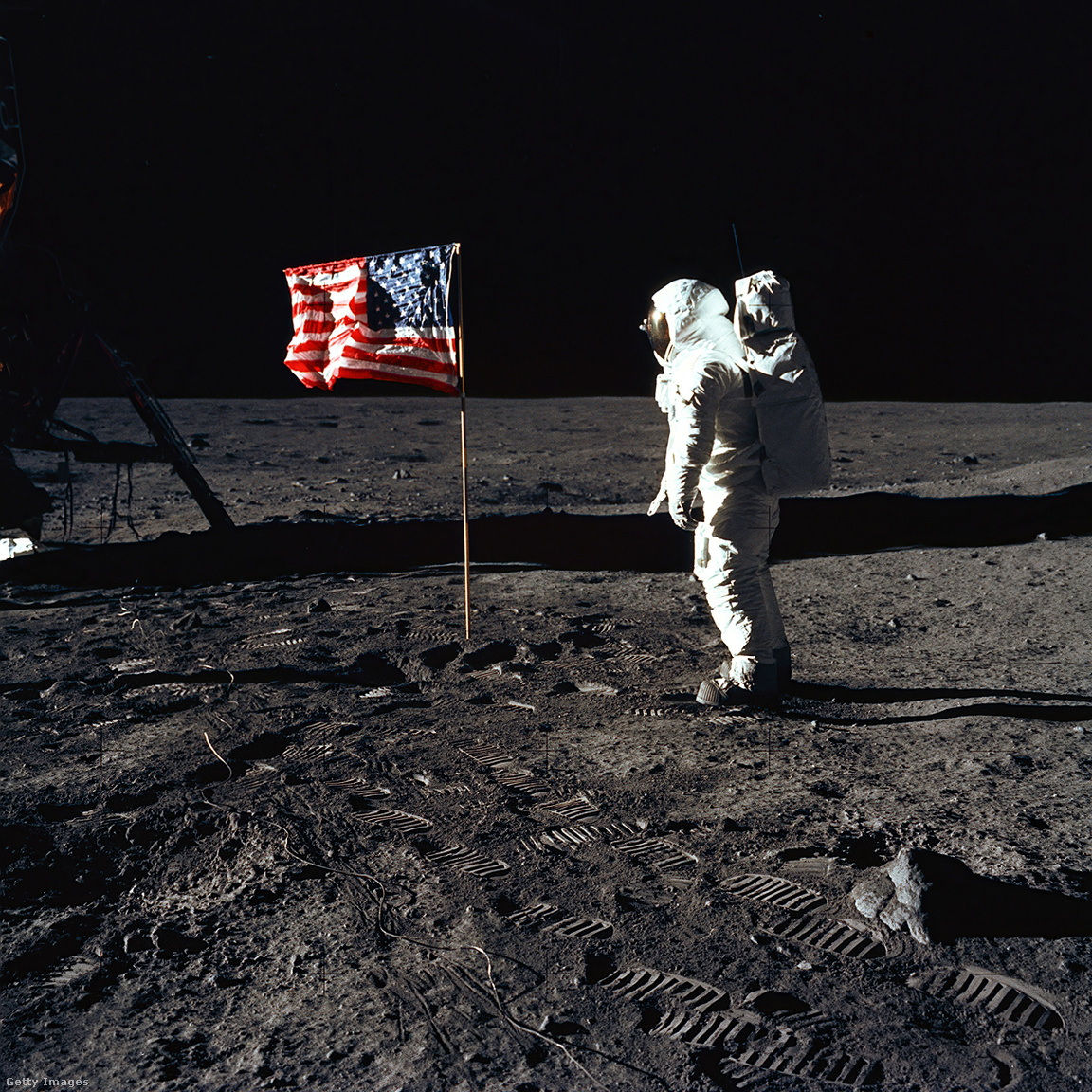 Edwin E. Buzz Aldrin Jr. űrhajós az Egyesült Államok zászlója mellett Holdséta közben. A Holdmodul a bal oldalon található, és az űrhajósok lábnyomai jól láthatóak a Hold talajában. Neil A. Armstrong űrhajós, az Apollo 11 parancsnoka ezt a képet egy 70 mm-es Hasselblad kamerával készítette
