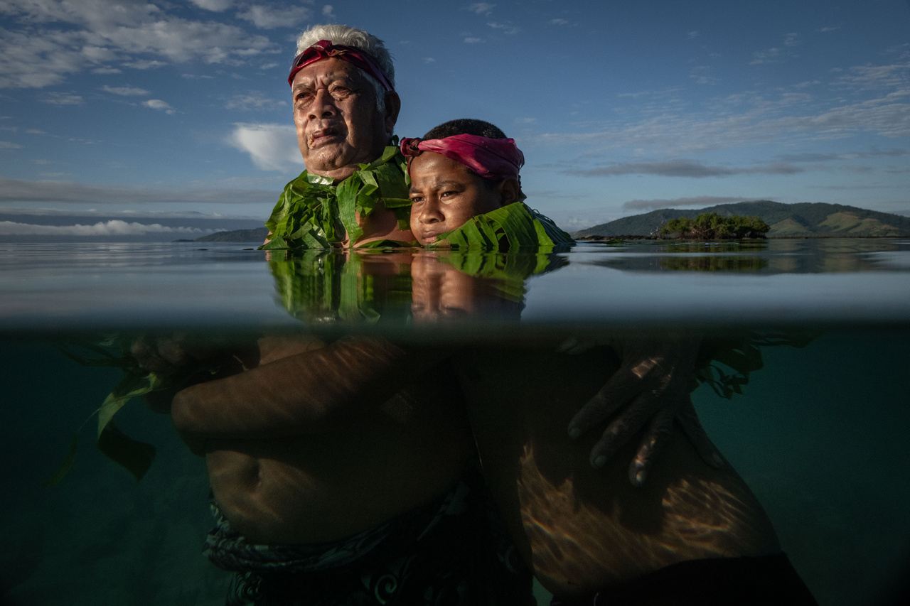 Nem süllyedünk el (Egyedi fotó - Délkelet-Ázsia és Óceánia) 
                        Lotomau Fiafia, a közösség rangidős tagja unokájával, Johnnal áll azon a ponton, ahol gyerekkorában még a partvonal volt. 
                        A Kioa-sziget 500 fős közössége olyan emberekből jött létre, akik az 1940-es években az északra fekvő Tuvalu szigetén kerestek menedéket a tengerszint emelkedése elől