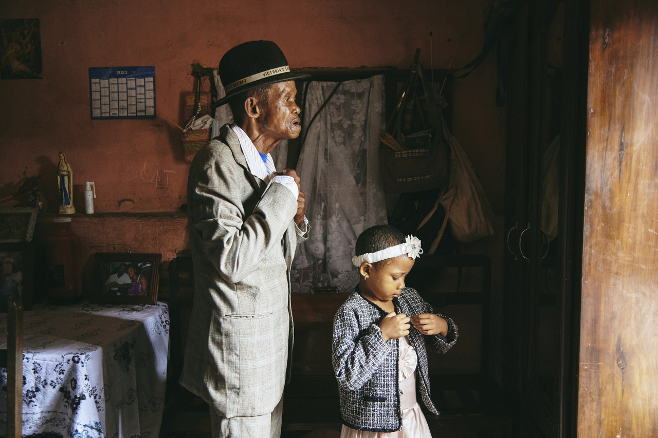 A Valim-babena történet (Fotósorozat - Afrika)
                        Madagaszkáron a demenciával összefüggő ismeretek hiánya miatt a memóriavesztés tüneteit mutató embereket gyakorta megbélyegzik. A demenciával élő 91 éves Paul Rakotozandrinyt, Dada Paul-t  évek óta lánya, Fara Rafaraniriana gondozza. Történetük jól illusztrálja a valim-babena elnevezésű madagaszkári szokást és elvet, ami azt jelenti, hogy a felnőtt gyermekek kötelessége a szülők támogatása.
                        A fotón Dada Paul és unokája, Odliatemix készülődnek a templomba. A férfi 11 éve szenved demenciában. Ez idő alatt családja sokáig azt feltételezte róla, hogy megőrült, a tüneteket az alkoholfogyasztásnak tulajdonították. Egyedül lánya, Fara vette észre, hogy valami megváltozott, és folytatta gondozását. Antananarivo, Madagaszkár, 2023. március 12.
                        
                         